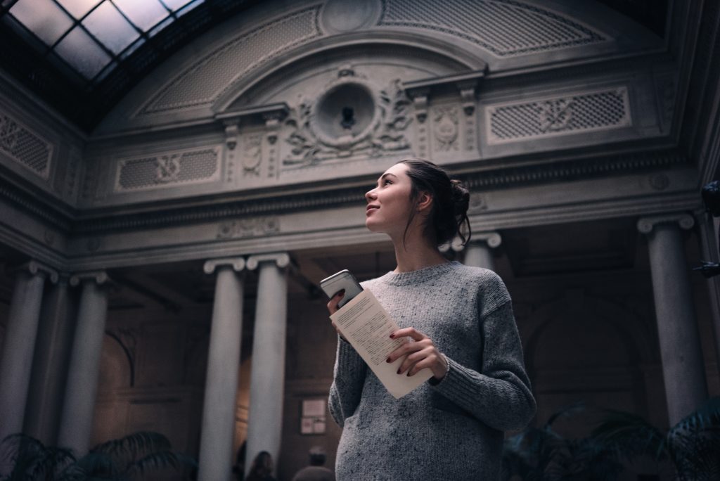 Portrait of a young woman tourist visiting museum or gallery, holding mobile phone