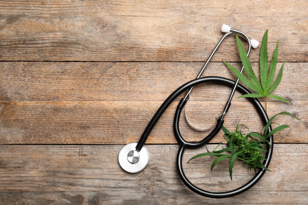 Hemp leaves and stethoscope on wooden background, flat lay. Space for text